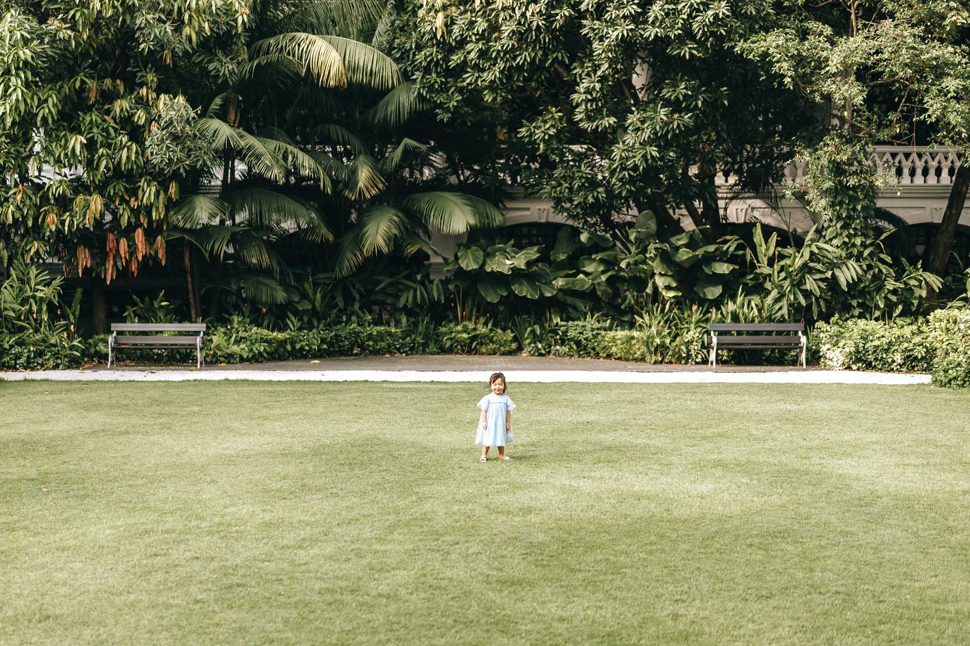 playful kid standing in the middle of the Raffles Hotel Lawn.