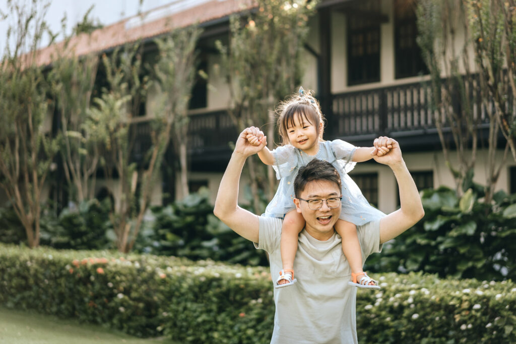 Father playing with his daughter over his shoulder during a photo shoot at the Raffles Hotel.